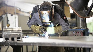 Mann mit Helm und Schutzkleidung vor Metallbauteil