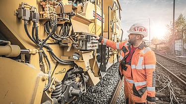 Mann mit Helm vor einem Schaltpanel eines Gleisbaugeräts