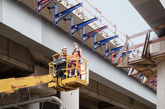Zwei Azubis begutachten eine Brücke aus einer Teleskophebebühne. 