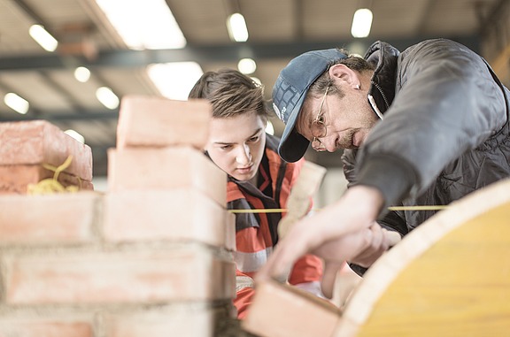 Auszubildender und Mentor bauen eine Mauer.