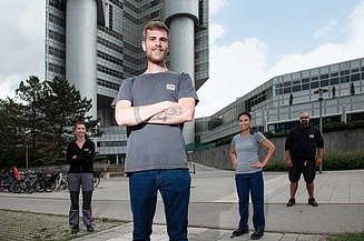 Junger Mann steht vor einem STRABAG Gebäude, im Hintergrund sein Team