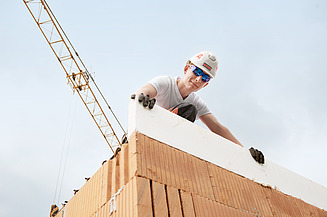 Azubi steht auf einer Mauer und blickt in die Kamera runter 