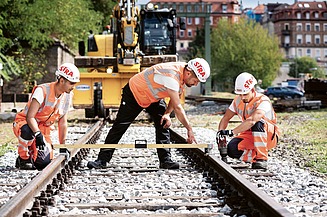 Junger Mann mit einem Gleisbaugerät vor einem Bagger