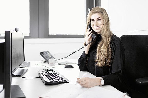 Auszubildende sitzt an ihrem Arbeitsplatz und telefoniert. 