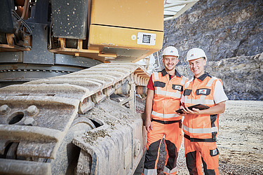 Foto Bauarbeiter stehen neben Bagger