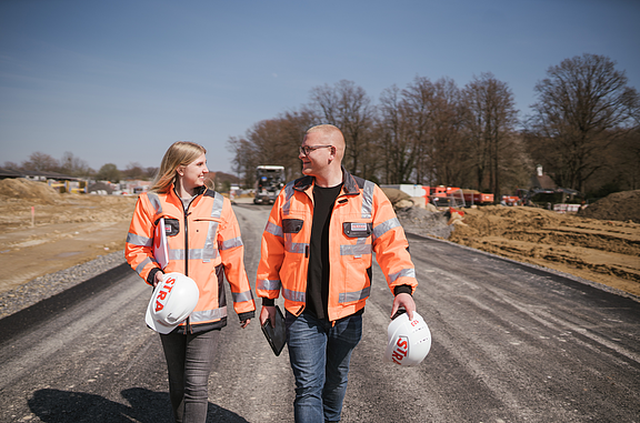 Zwei Studierende laufen auf einer Baustelle und schauen sich an.