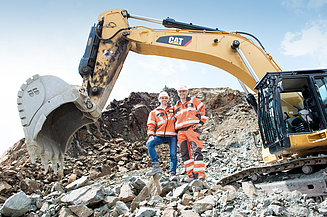 Foto mit 2 Personen, die vor einem Bagger im Steinbruch stehen