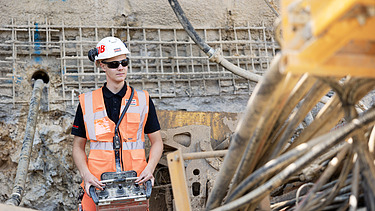 Ausbildung als Spezialtiefbauer:in Azubi steuert ein Baugerät auf einer Baustelle mit Fernbedienung