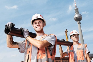 Foto Ausbildung Kanalbau Zwei Azubis tragen ein Rohr auf einer Baustelle