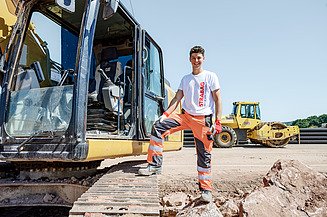 Zwei Facharbeiter stehen auf einem Asphaltfertiger und bauen Asphalt ein