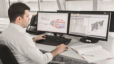 Mann arbeitet an zwei Bildschirmen mit Bauzeichnungen